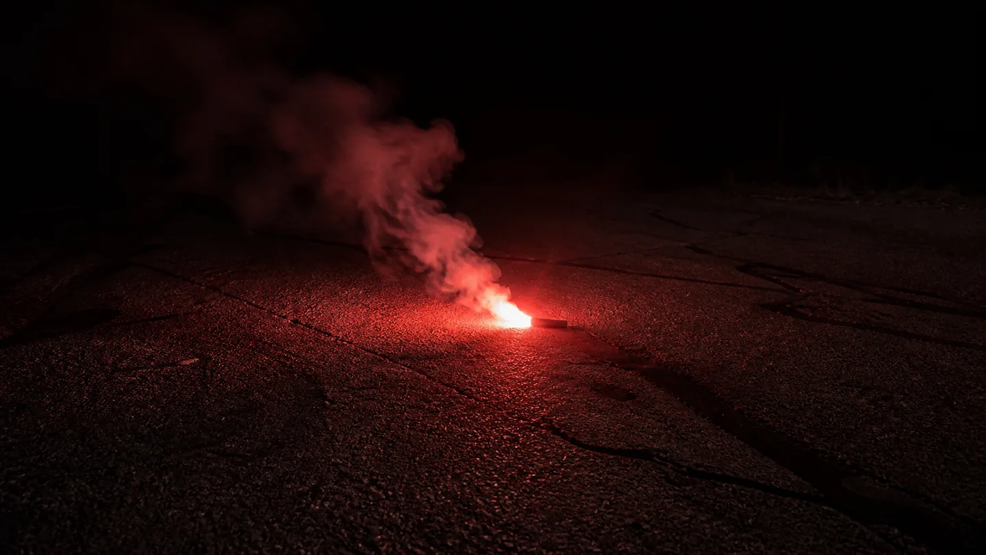 A red road flare burning alone on cracked asphalt at night